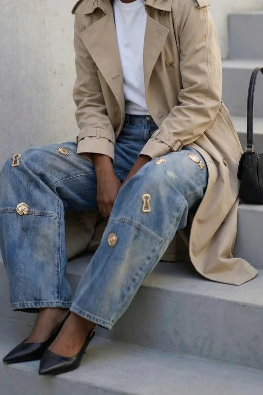 Gold charm jeans worn sitting on stone steps, curved barrel leg