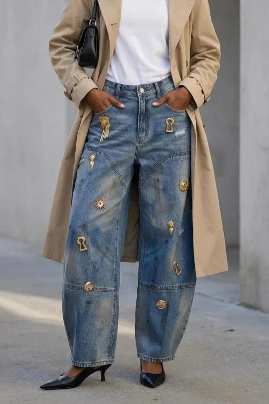 Embellished jeans for women with gold charms on a barrel leg, front view with trench coat