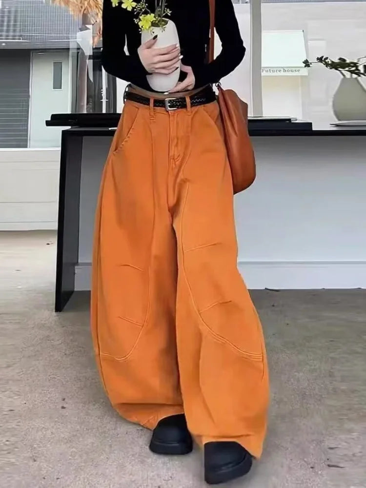 Orange barrel pants three quarter view, full length hem over black boots