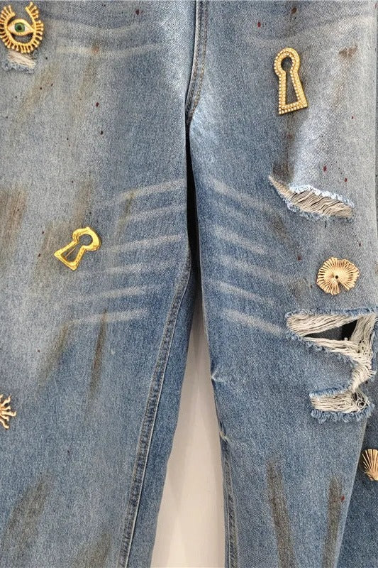 Close up of gold metal charms and distressing on mid blue denim