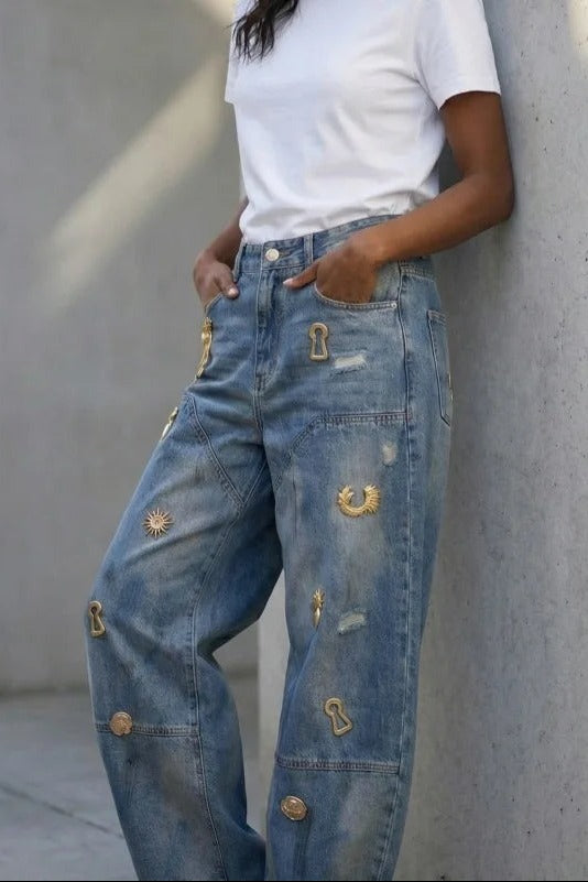Embellished barrel jeans leaning against wall, side view showing charm placement