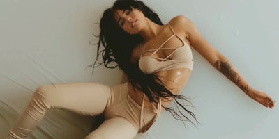 A TGC Boutique model, woman with long, wet black hair lies on a light surface, wearing a strappy beige top and matching pants. 