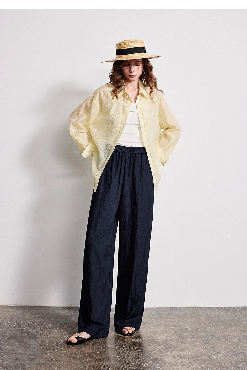 Woman in a straw hat and yellow shirt wearing navy wide leg trousers with flat sandals
